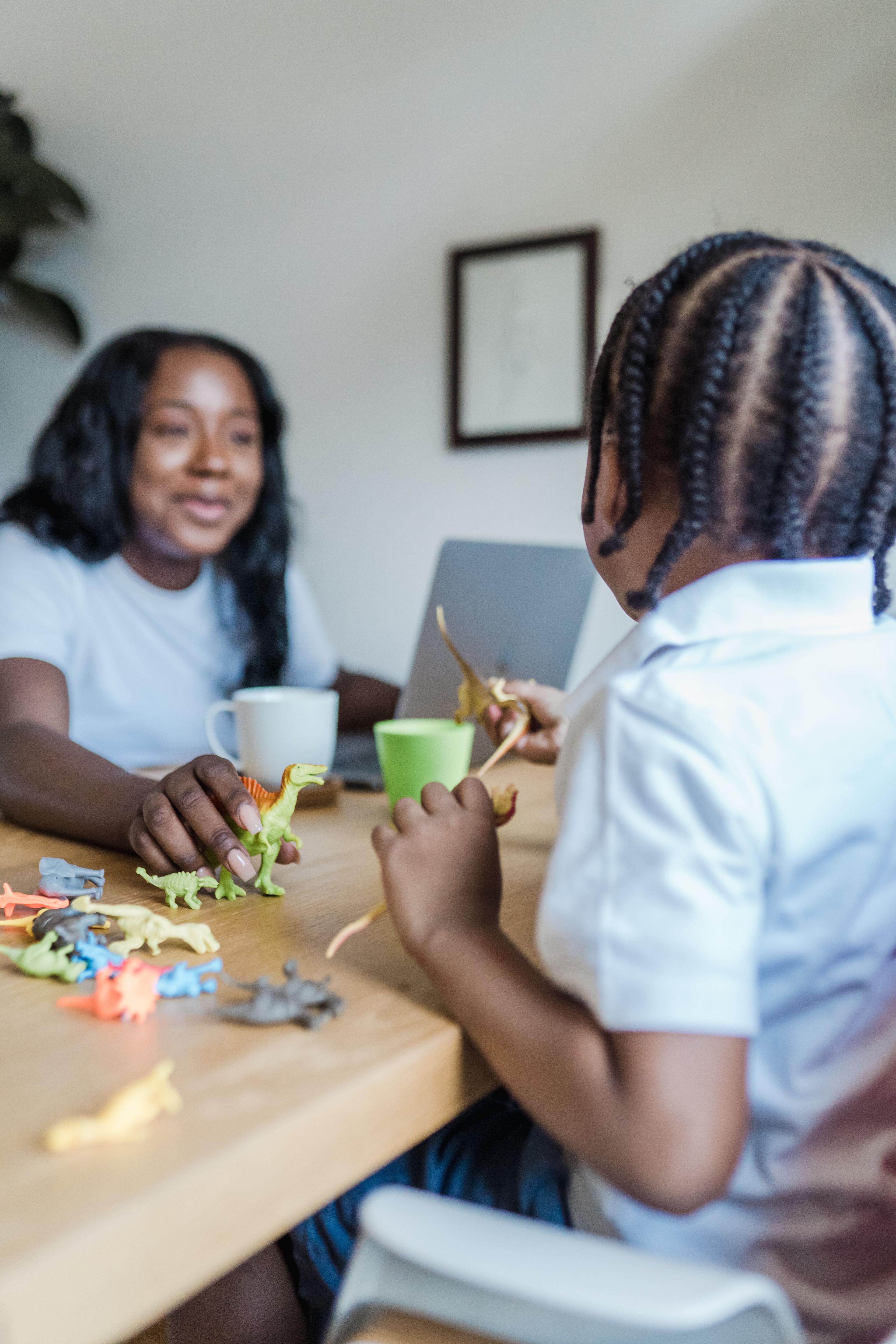 A woman and child play with dinosaur figures at a table.