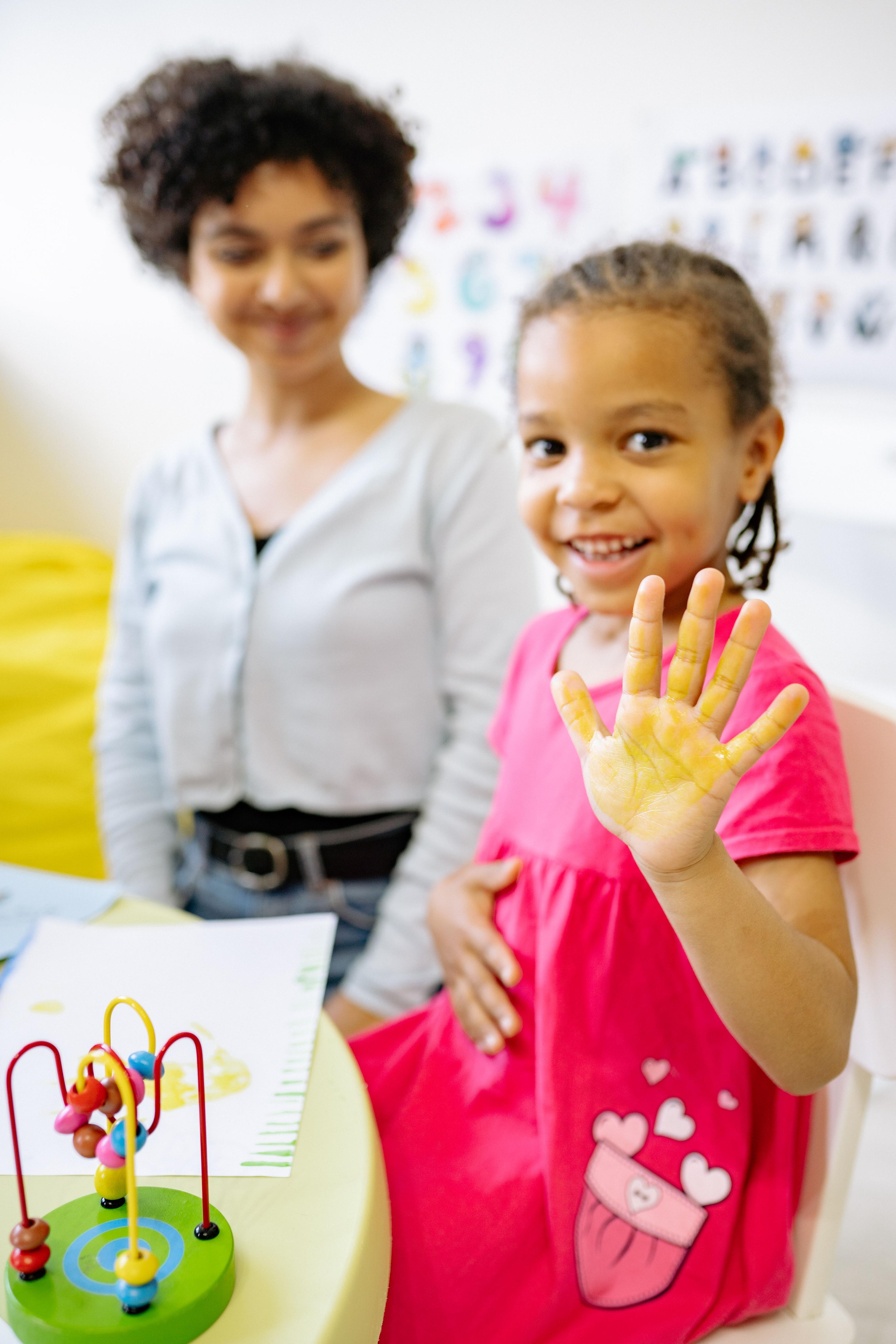 A smiling child showing an adult her yellow-painted hand